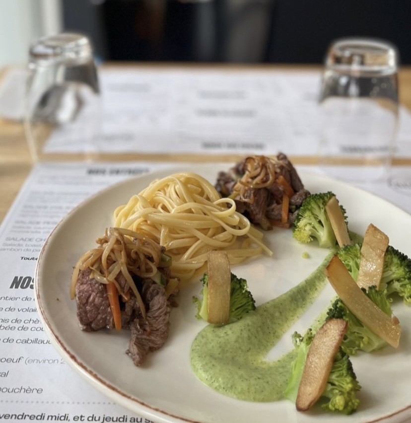back view of woman wearing a backpack and beanie waiting to cross the road on a busy street at night in New York City, USA